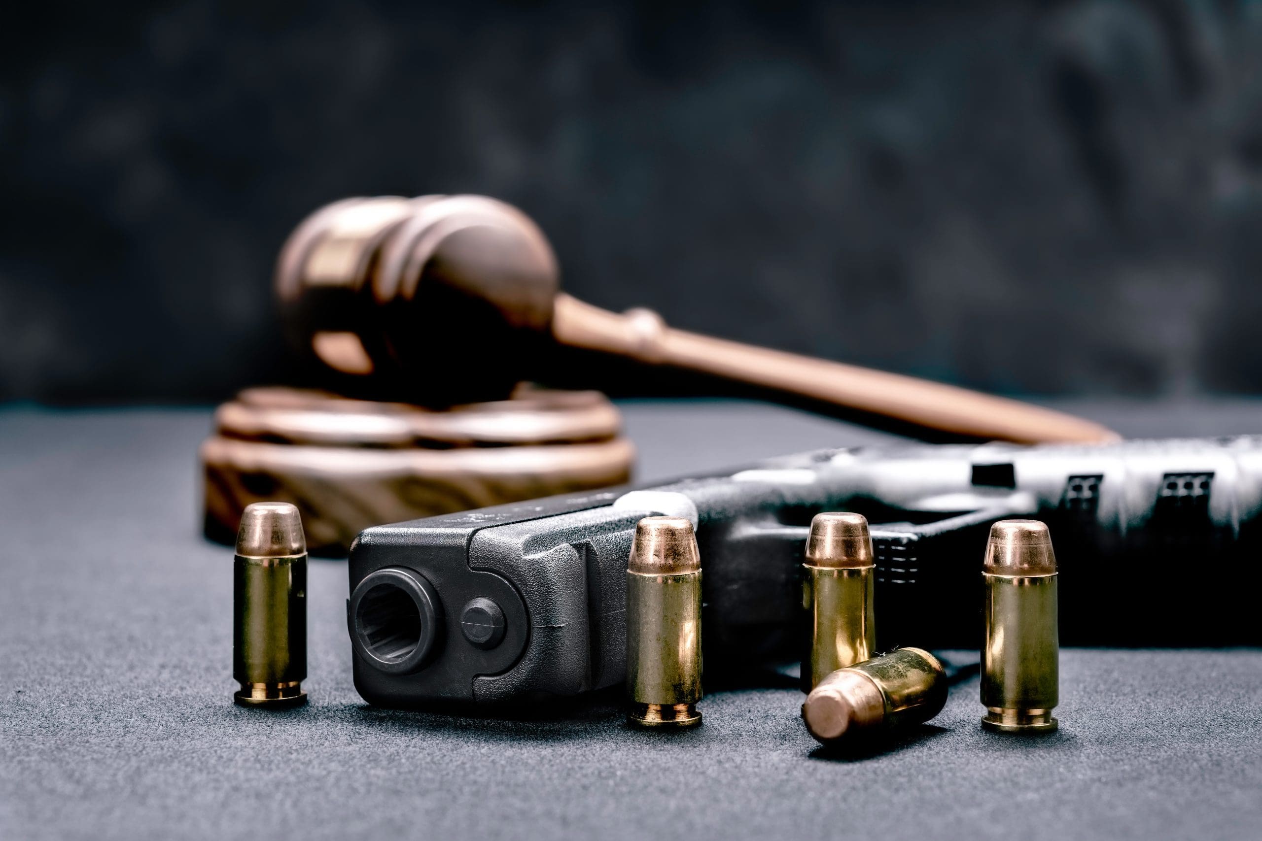 A gun and bullets on a table with a judge's gavel.