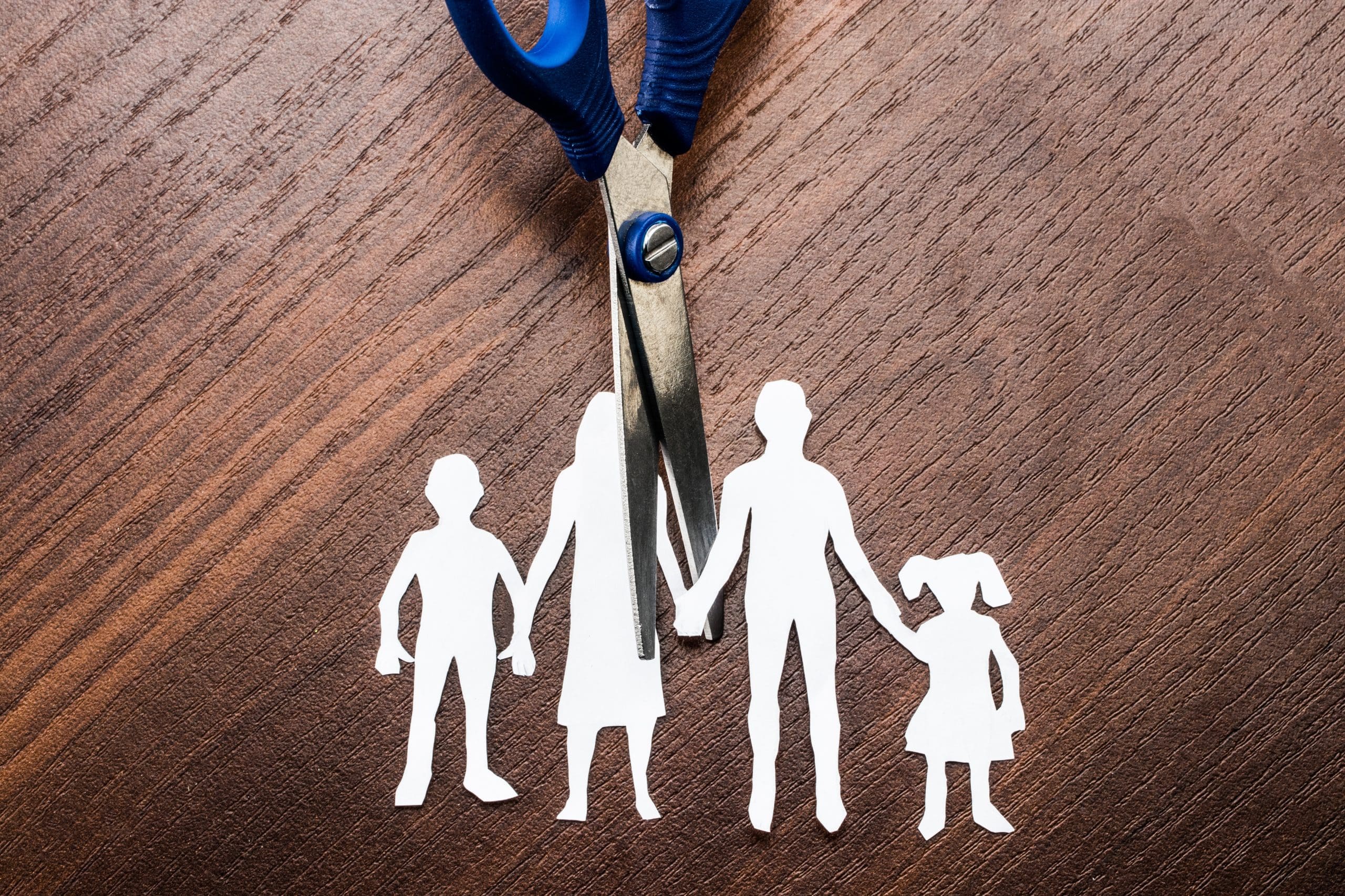A pair of scissors with a family silhouette on a wooden table.