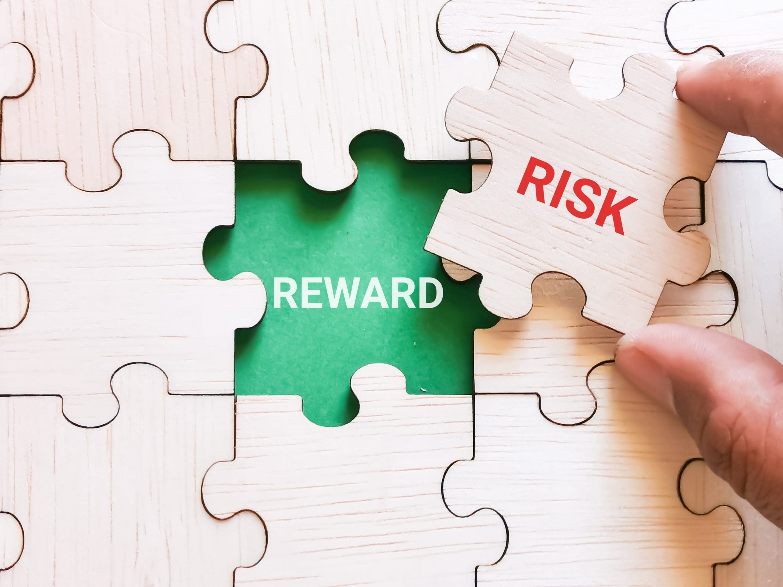 A person putting a piece of jigsaw puzzle with the word risk and reward.