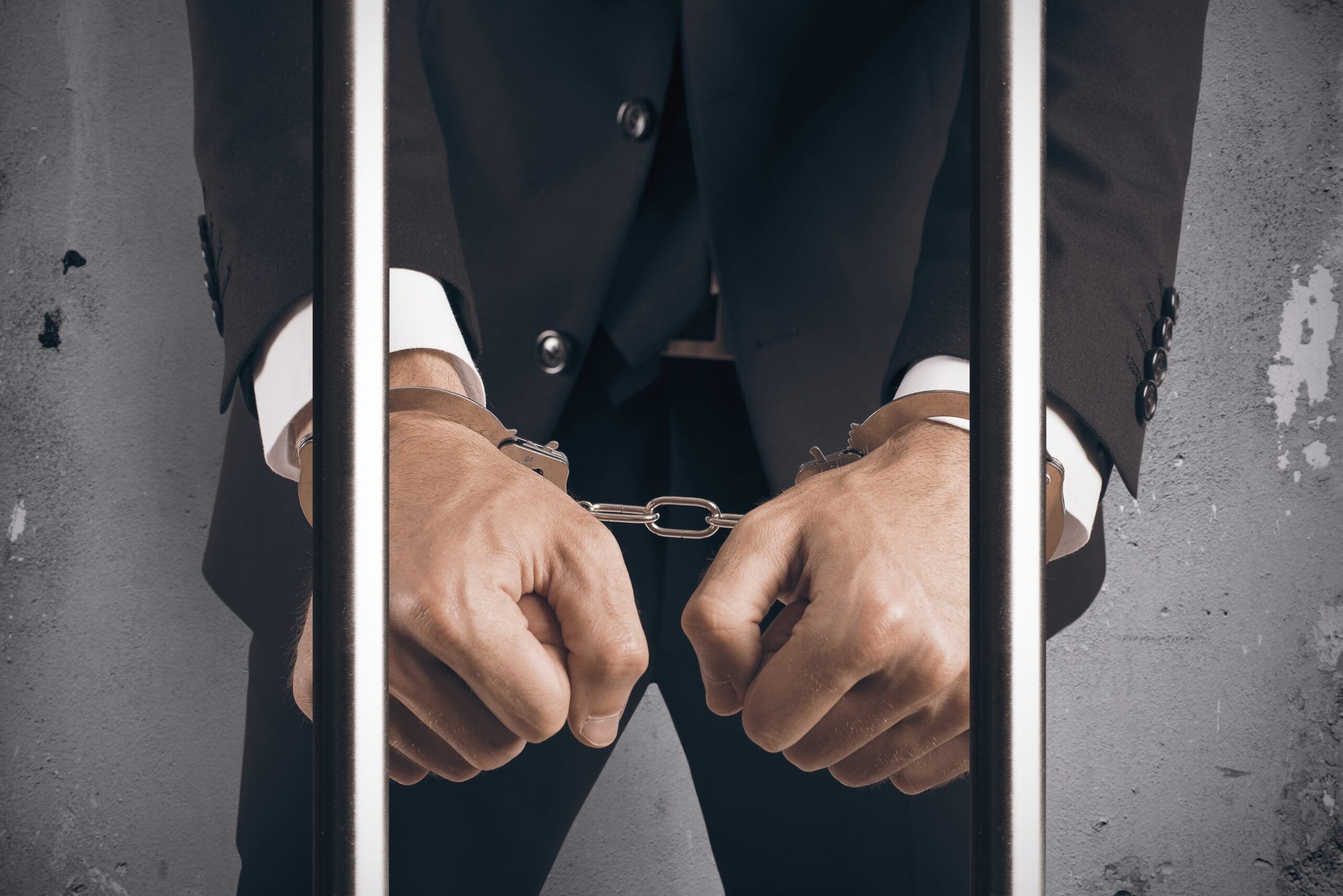 A man in handcuffs behind bars.